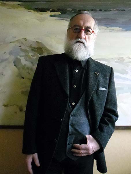 The artsit Joseph J. Visser in a black suit standing in front of one of his paintings